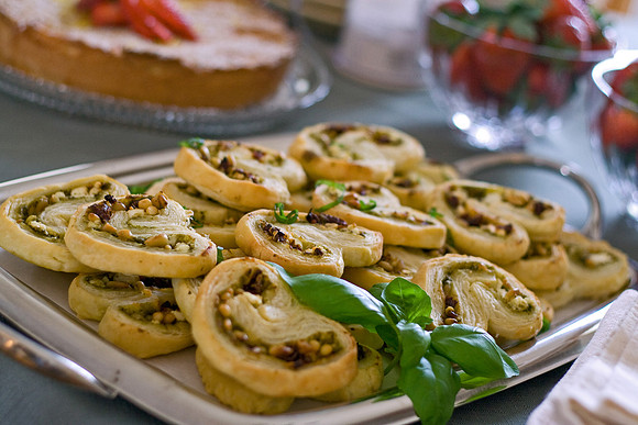 Palmiere - flaky puff pastry is spread with basil pesto, sun-dried tomatoes, crumbled goat cheese and pine nuts, folded, sliced and baked